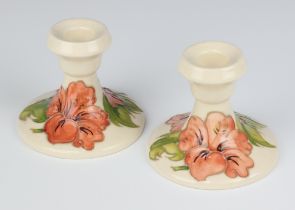 A pair of Moorcroft white glazed candlesticks of waisted form decorated the hibiscus pattern, base