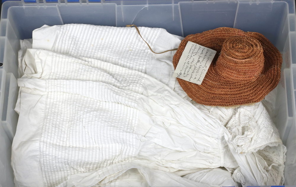 Six Victorian white cotton christening gowns and a collection of fabrics in a white plastic trunk