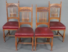 A set of 4 Art Nouveau oak stick and rail back dining chairs, the seats upholstered in red