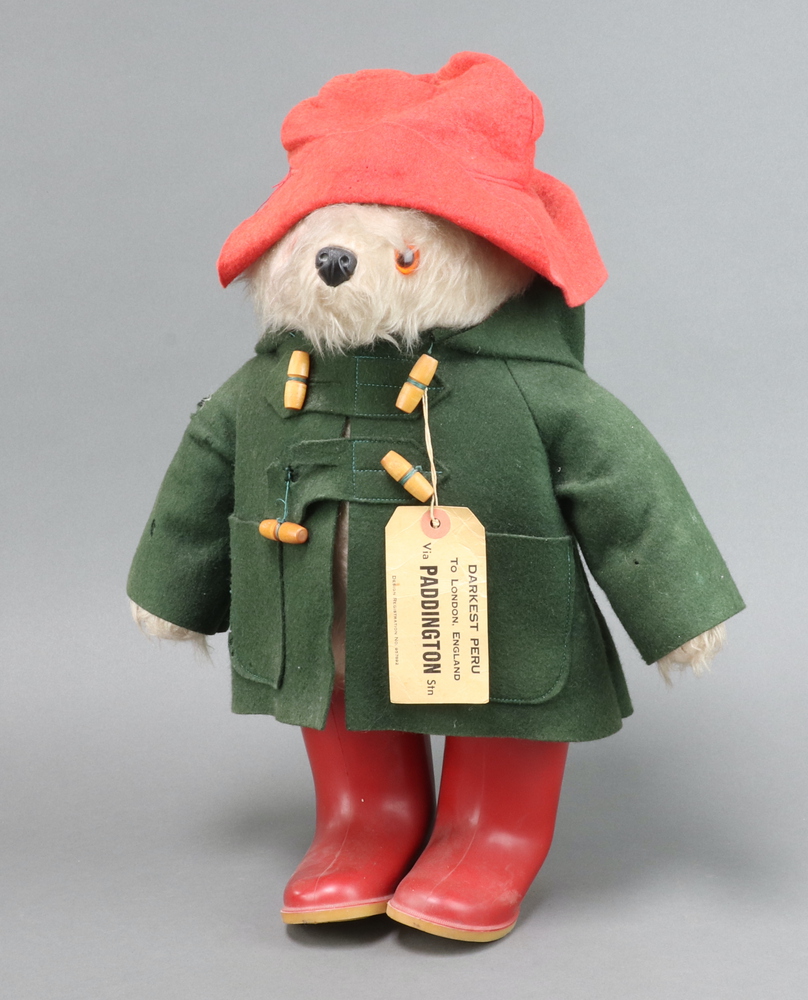 A Paddington Bear with red Dunlop boots, label attached to green duffle coat and red hat There is