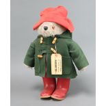 A Paddington Bear with red Dunlop boots, label attached to green duffle coat and red hat There is