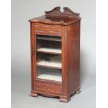 An Edwardian music cabinet with shaped top, fitted shelves enclosed by glazed panelled door,