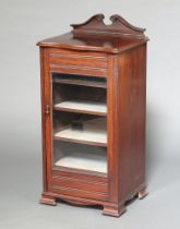 An Edwardian music cabinet with shaped top, fitted shelves enclosed by glazed panelled door,