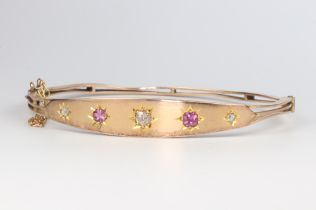 A 9ct yellow gold diamond and ruby bangle, the 3 diamonds 0.20ct, the 2 rubies 0.30ct, 50mm diam., 7