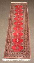 A red and brown ground Bokhara runner with 9 octagons the centre within a multi row border 323cm x