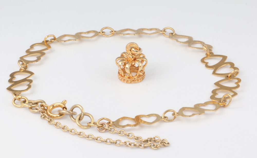 A yellow metal charm in the form of a crown together with a yellow metal bracelet of heart shaped