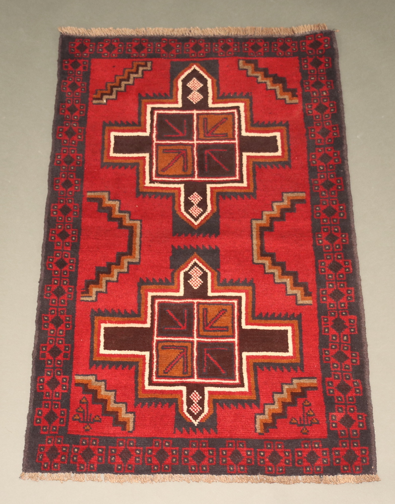 A red, black and white ground Belouche rug with 2 medallions to the centre 136cm x 87cm