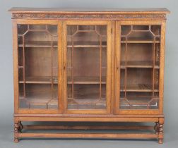 A 1920's carved oak bookcase with carved frieze enclosed by triple astragal glazed panelled door, on