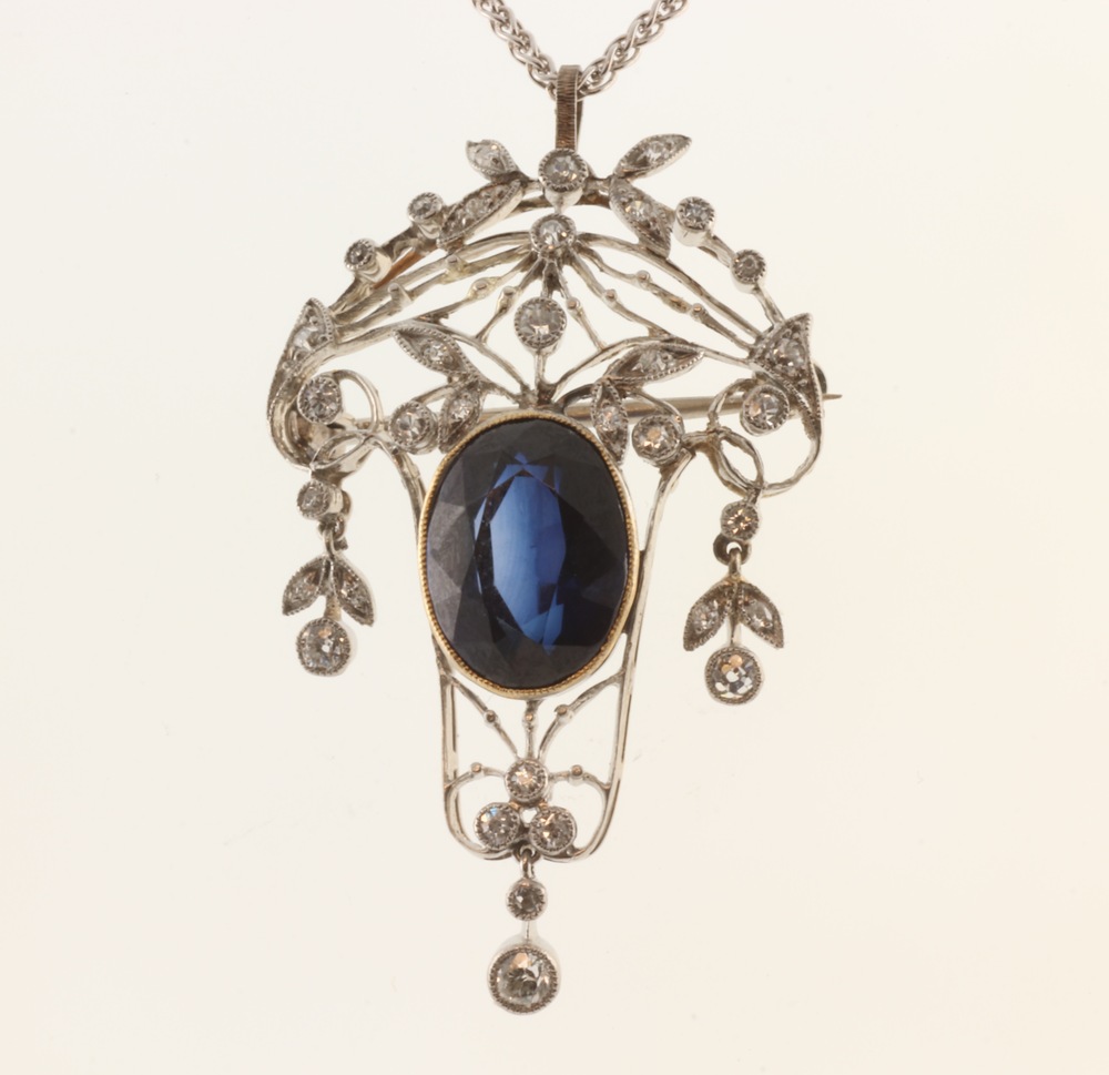 An Edwardian style synthetic sapphire and diamond white metal pendant brooch, the oval cut centre