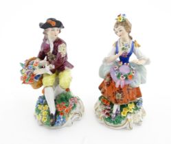 A pair of Sitzendorf figures, comprising a seated male figure with a basket of flowers and seated
