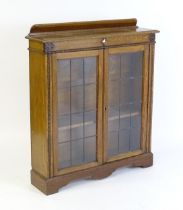 A mid 20thC oak glazed bookcase with a shaped upstand above carved detailing with beadwork mouldings