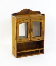 A pine hanging wall cabinet, with two glazed doors above a small rack with a gallery of turned