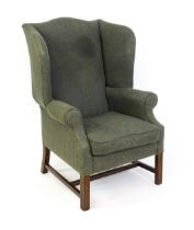 An early 20thC wingback armchair raised on chamfered front legs united by a H stretcher. 33" wide