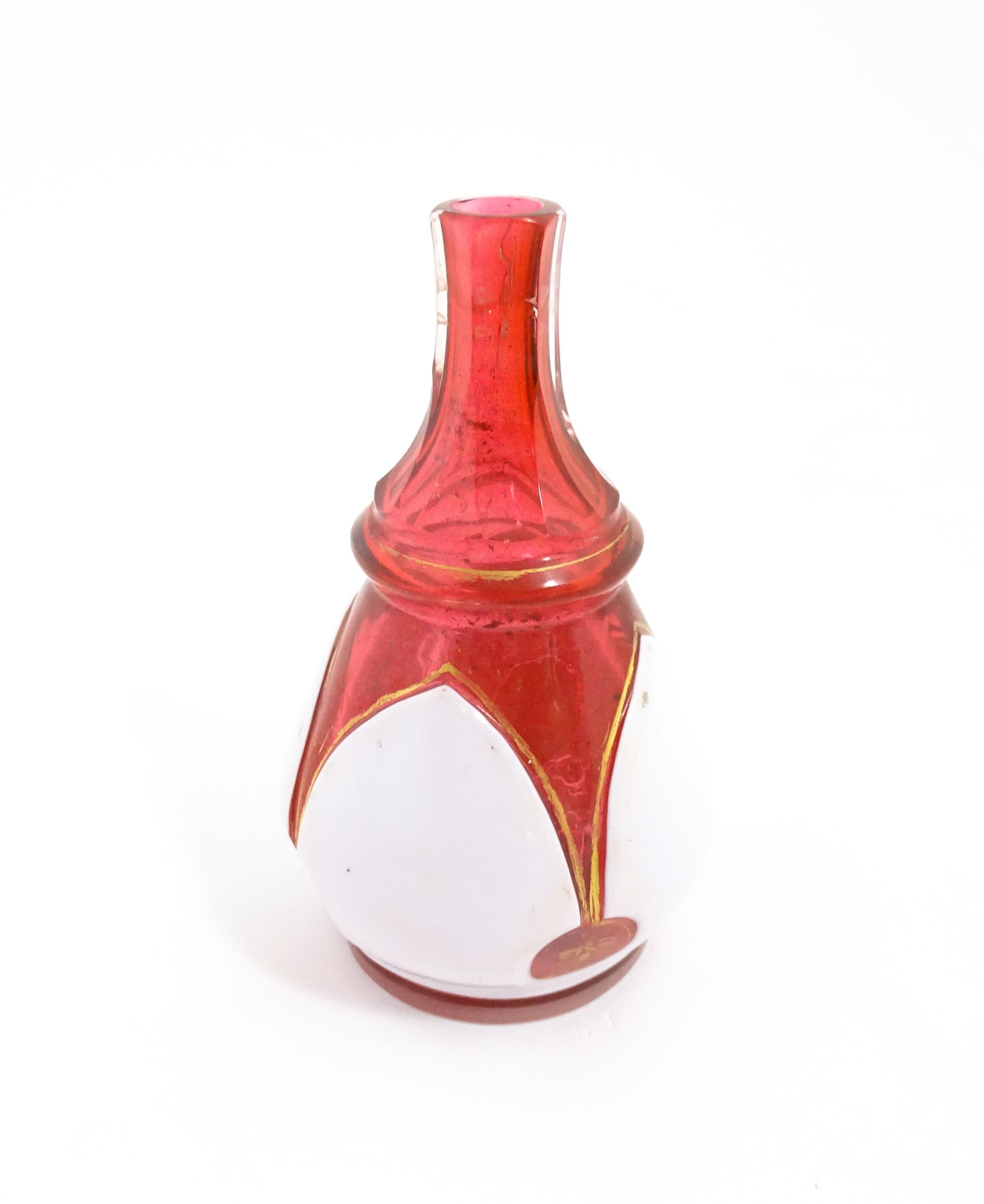 A small Bohemian style red and white glass bottle vase with gilt highlights. Approx. 3 3/4" high