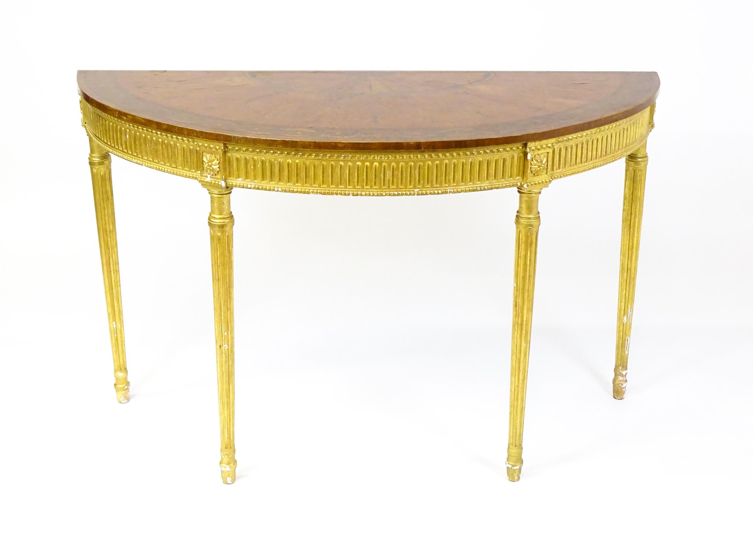 A demi lune console table with a marquetry inlaid top above a fluted frieze and moulded floral