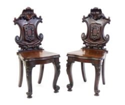 A pair of Victorian mahogany hall chairs with heavily carved tops above waisted backrests with