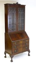 An early 20thC mahogany bureau bookcase with a carved cornice above two astragal glazed doors and