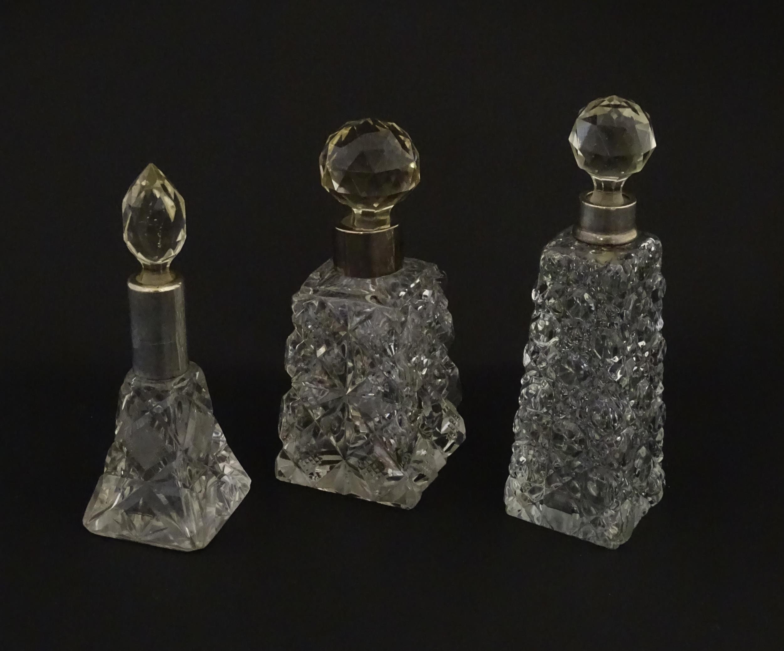 Three assorted cut glass scent / perfume bottles with silver mounts, to include one hallmarked