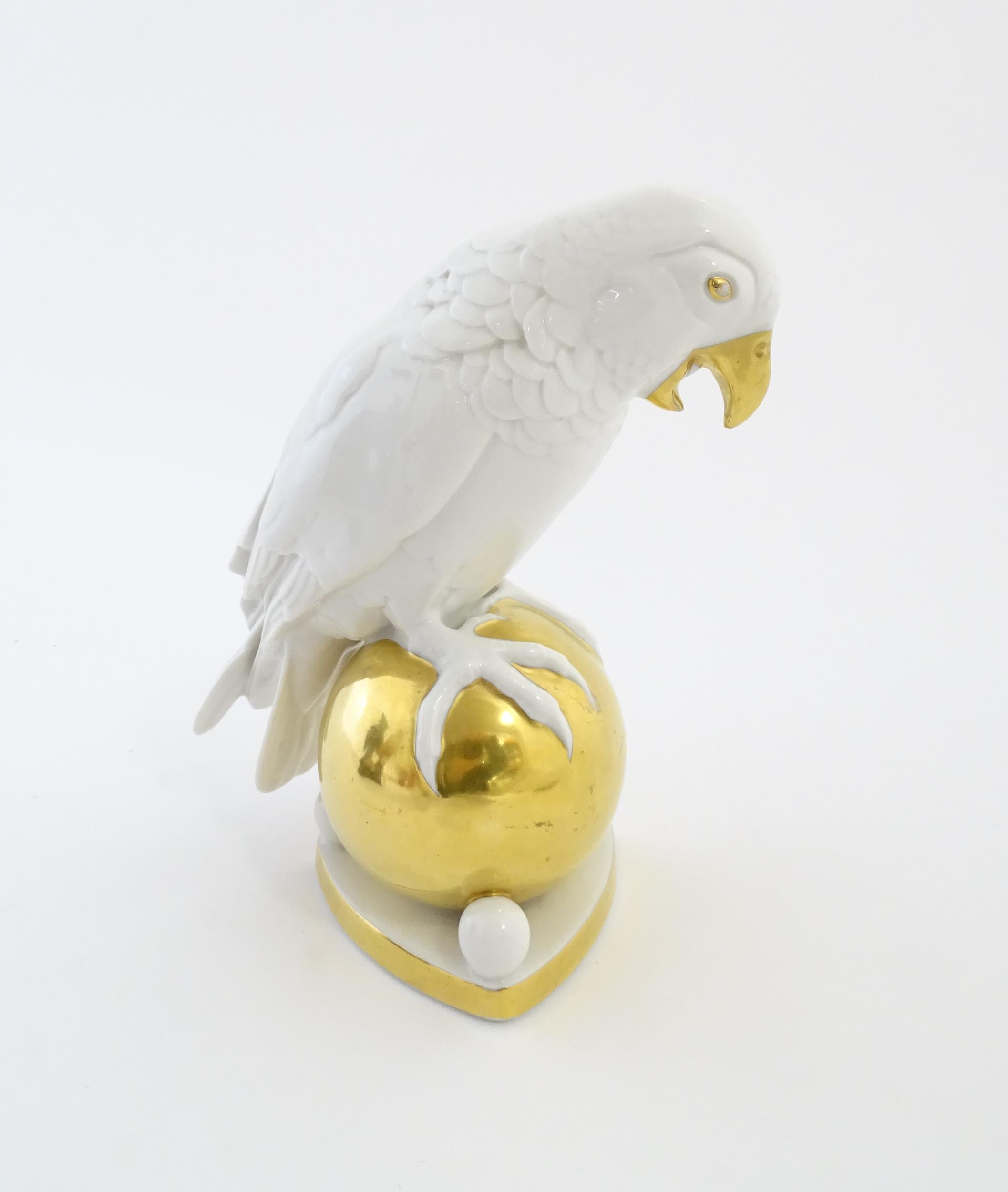 A Hutschenreuther model of a parrot perched upon a gilt ball. Marked under. Approx. 8 1/4" high
