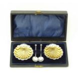 A pair of silver salts of scallop shell form with gilded interiors with two salt spoons. All
