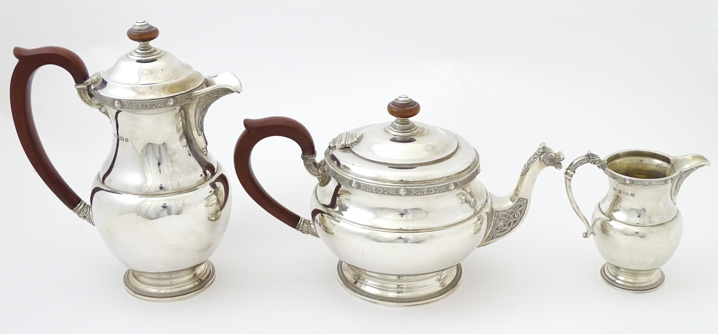 A three piece silver tea set comprising teapot, hot water pot and cream jug, with Celtic style