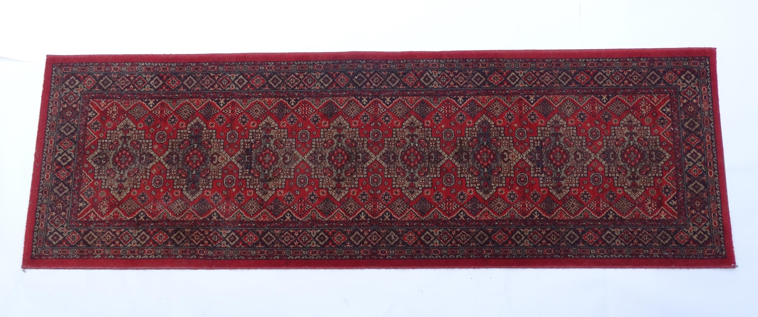 Carpet / Rug : A red ground runner with repeating motifs to centre, bordered by geometric banding.