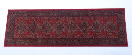 Carpet / Rug : A red ground runner with repeating motifs to centre, bordered by geometric banding.