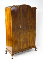 An Art Deco style walnut wardrobe with a shaped cornice above a single panelled door raised on a