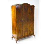 An Art Deco style walnut wardrobe with a shaped cornice above a single panelled door raised on a
