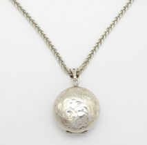 A silver pendant of locket form with engraved foliate decoration. With a silver chain. Locket