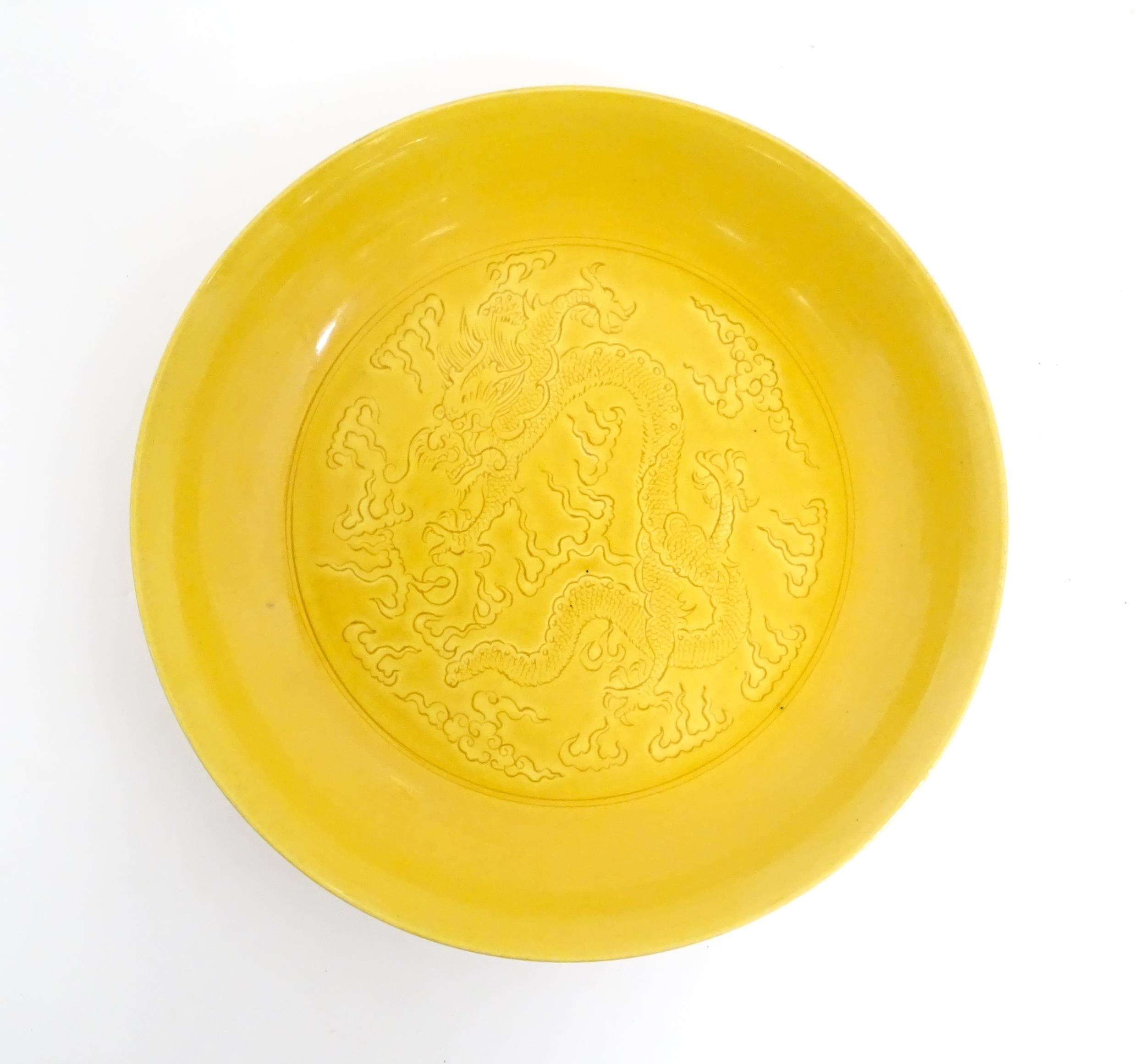 A Chinese dish with a yellow ground decorated with dragons amongst stylised clouds. Character