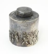 A silver tea caddy depicting a village scene with buildings and figures. Hallmarked Chester c.