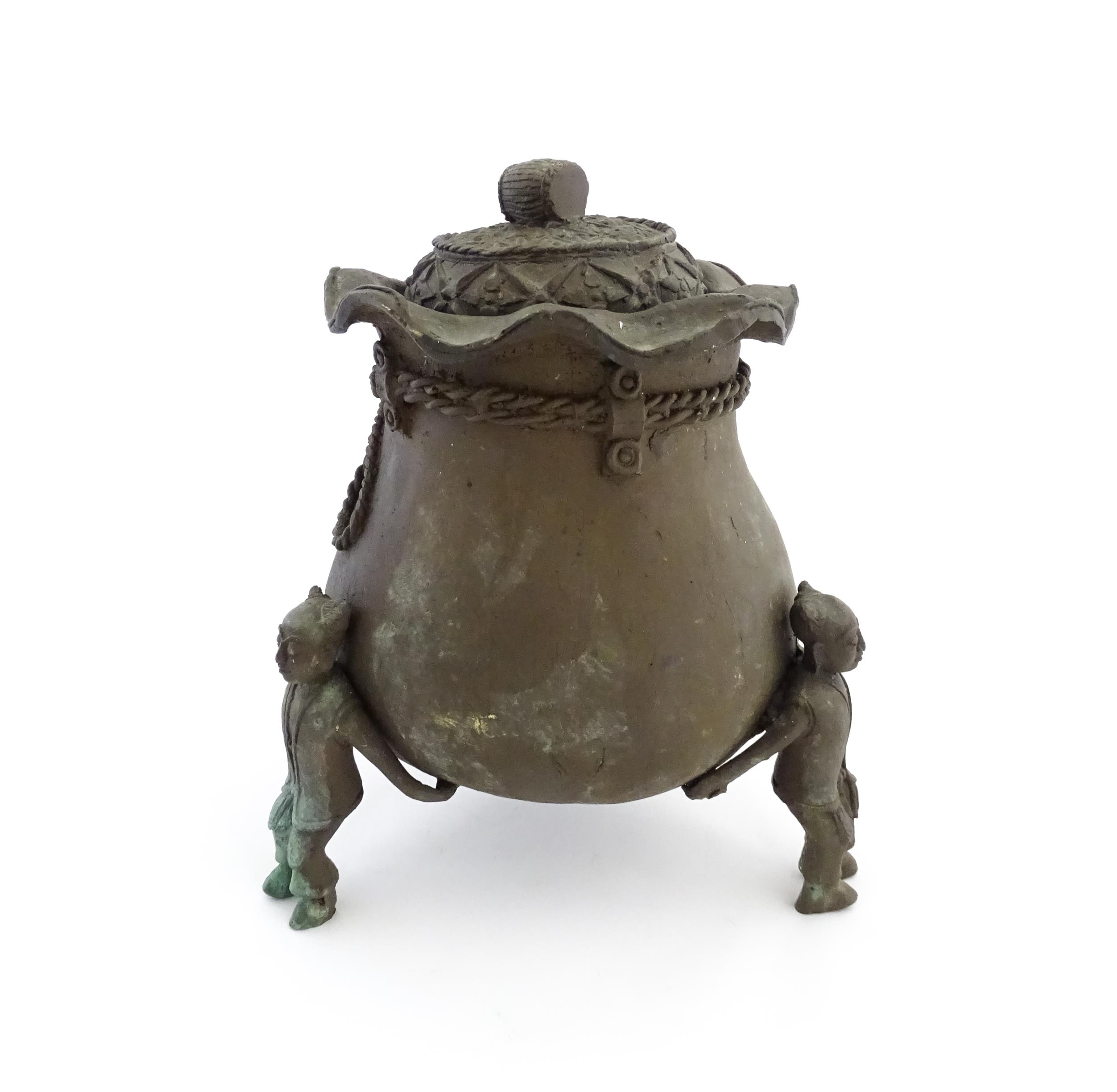 A Chinese cast bronze pot and cover modelled as a money bag with rope tie supported by three figural