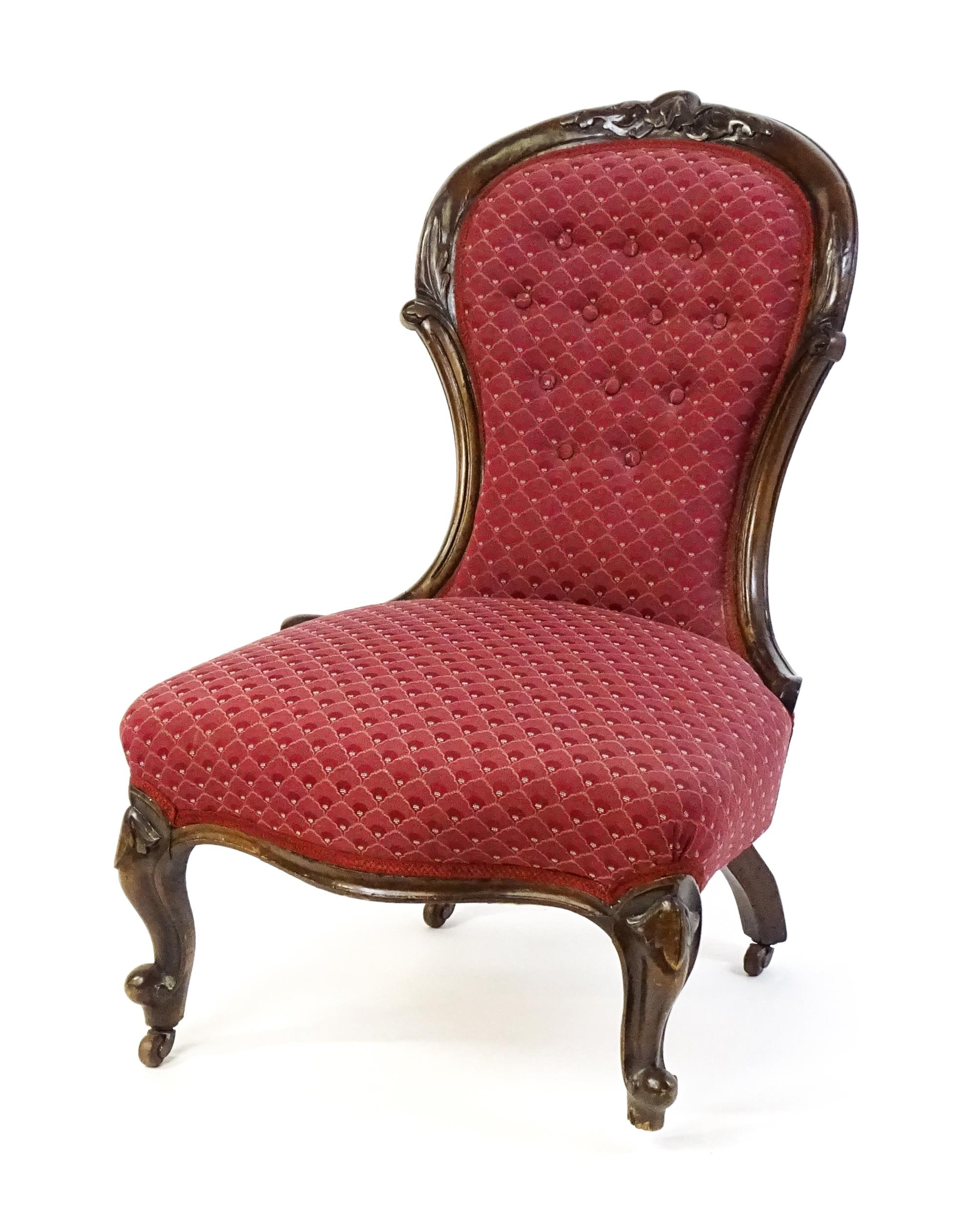 A late 19thC / early 20thC nursing chair with a deep buttoned spoon back adorned with a carved