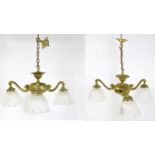 A pair of brass pendant lights having three scrolling branches with three holophane shades.