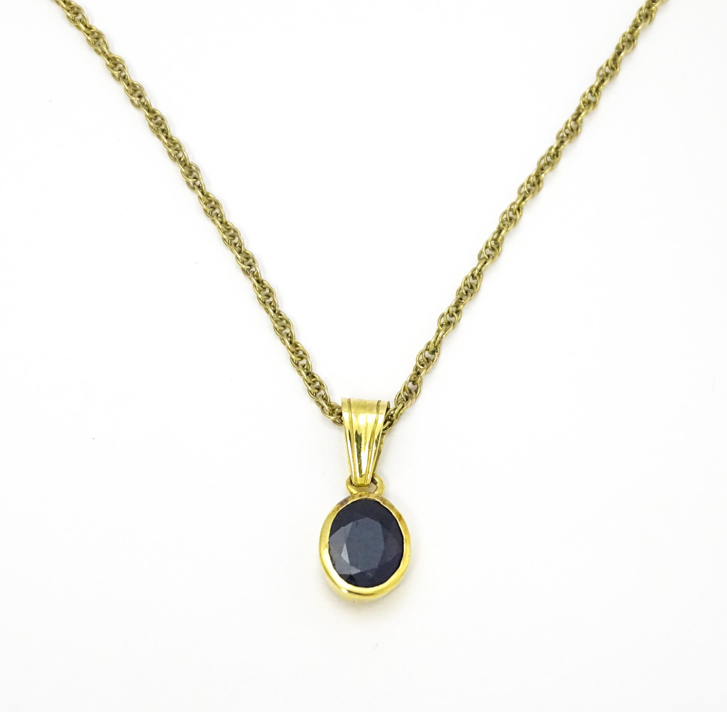 A yellow metal pendant set with central sapphire on a 9ct gold chain. Pendant approx. 1 3/4" long