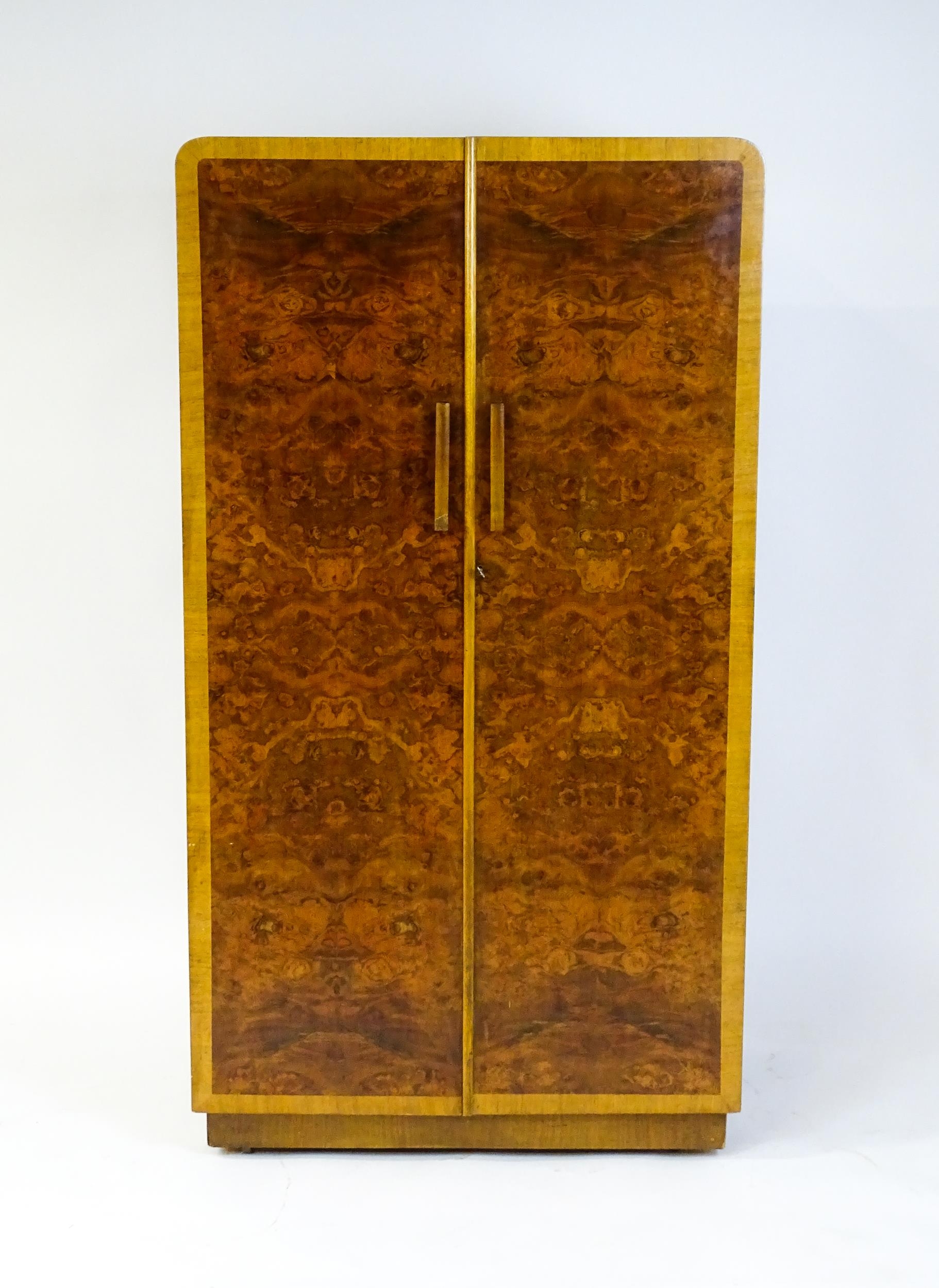 A mid 20thC Art Deco style wardrobe / cupboard with burr walnut veneered doors and shaped handles.