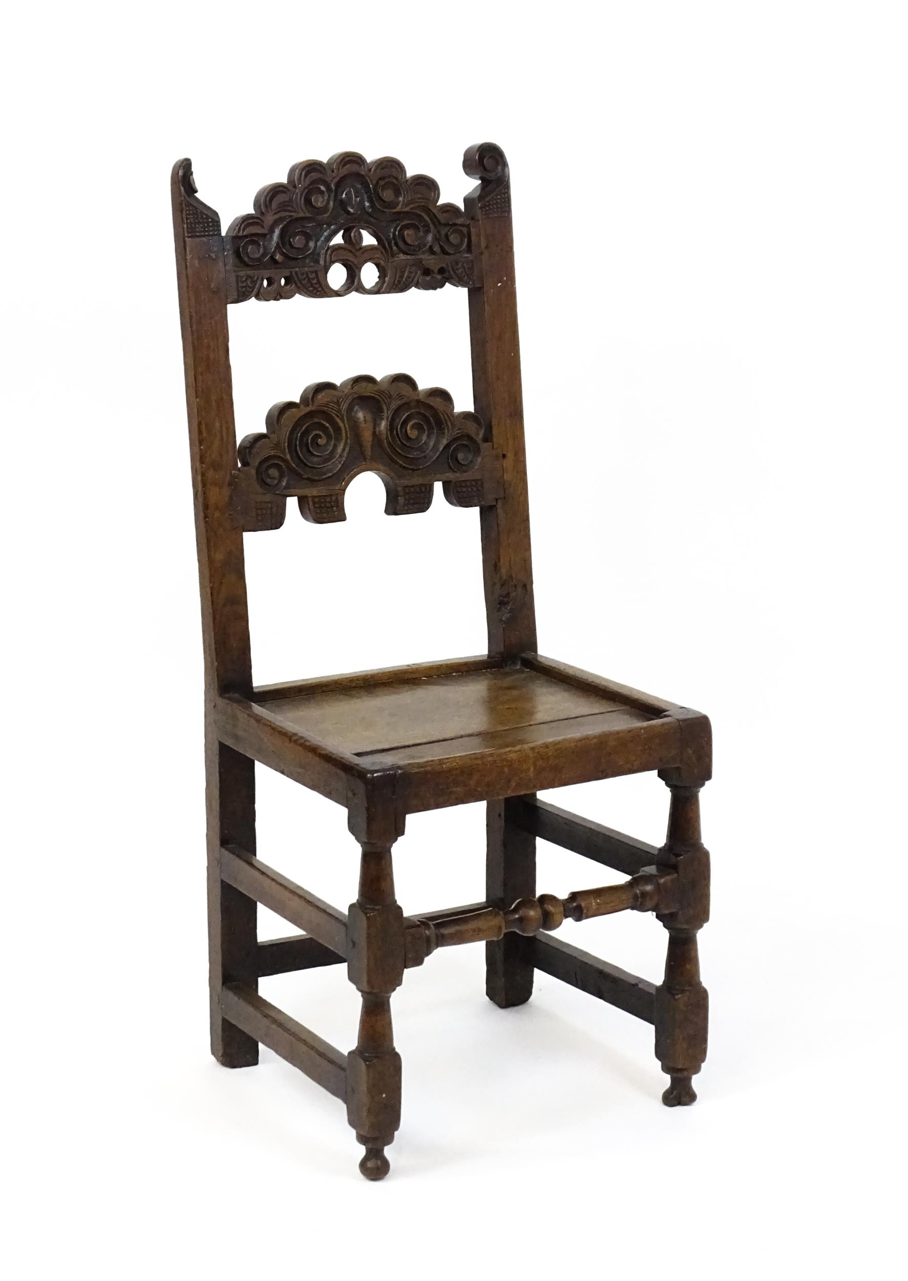 A 17thC oak peg jointed hall chair / back stool with a carved and scrolled top and mid rail raised