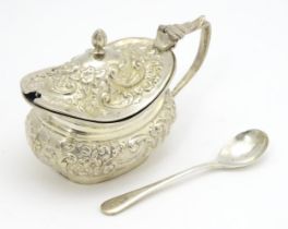 A silver mustard pot with embossed foliate decoration and blue glass liner, hallmarked Birmingham