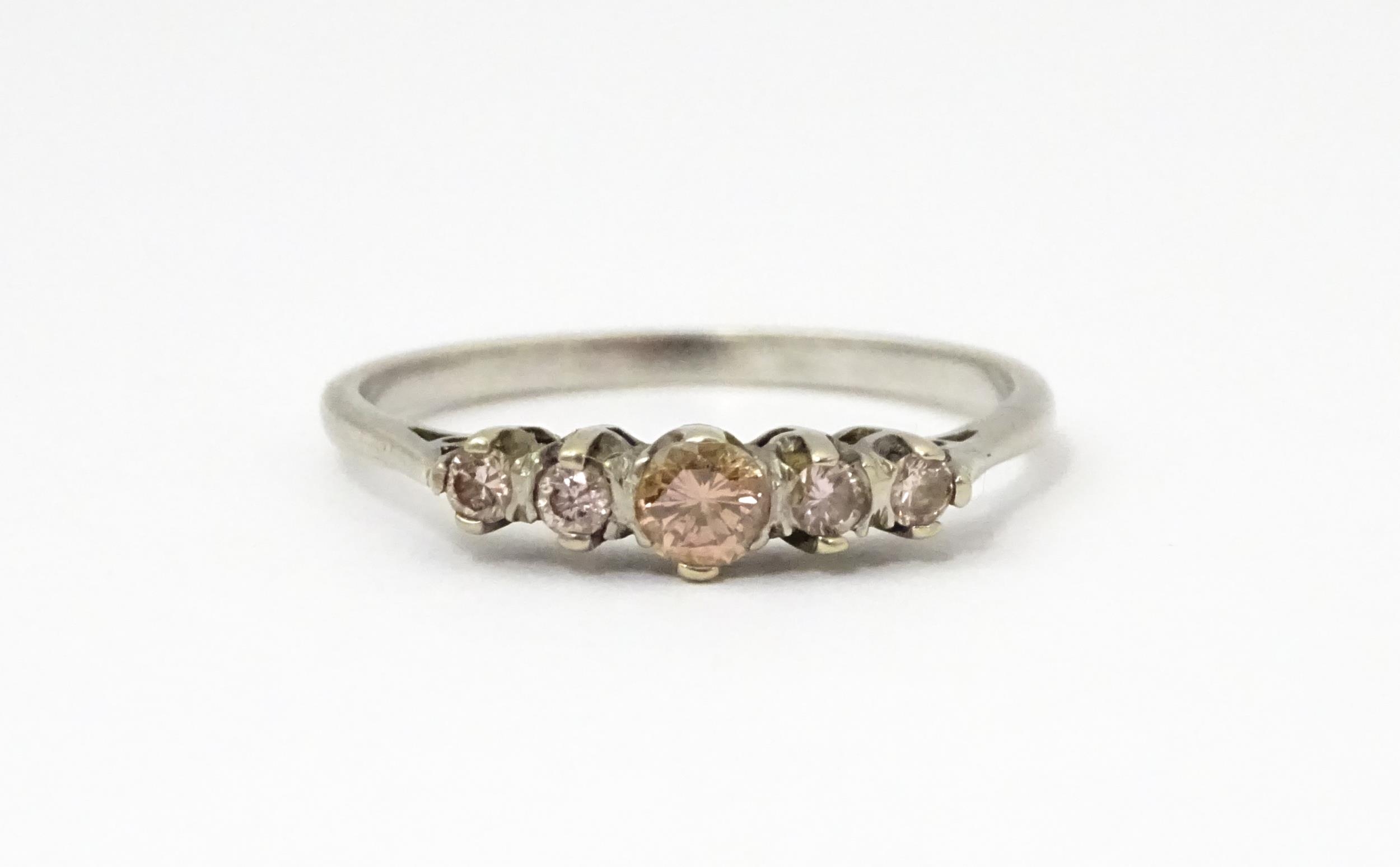 A white gold ring set with central brown diamond flanked by 4 further diamonds in a linear