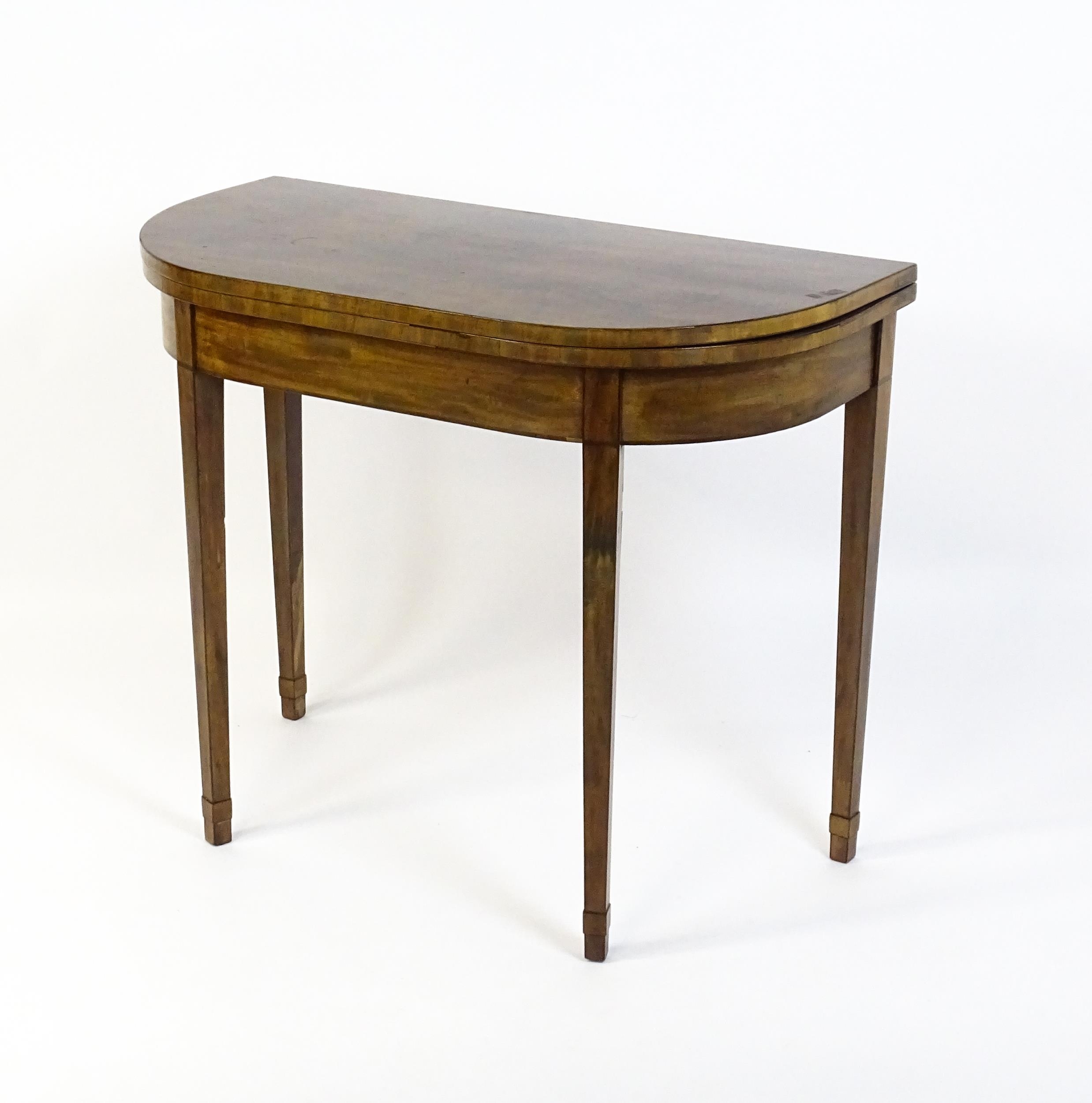 An early 19thC mahogany card table of demi lune form, the top opening to show a baize circular