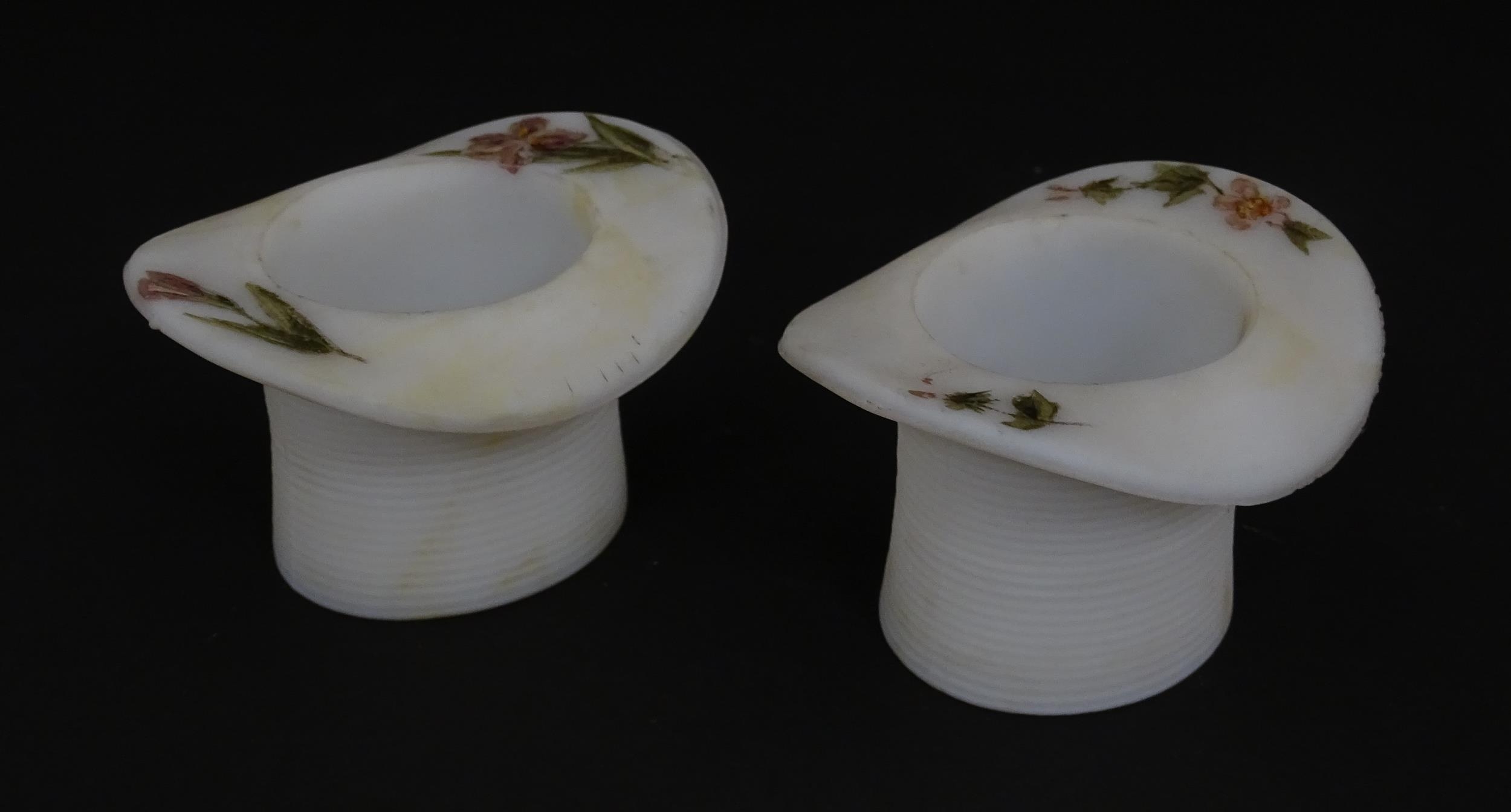 A pair of milk glass match holders / vesta keeps formed as top hats with hand painted floral detail.