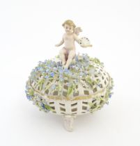 A Continental basket and cover with pierced detail and encrusted flowers surmounted by a putto /