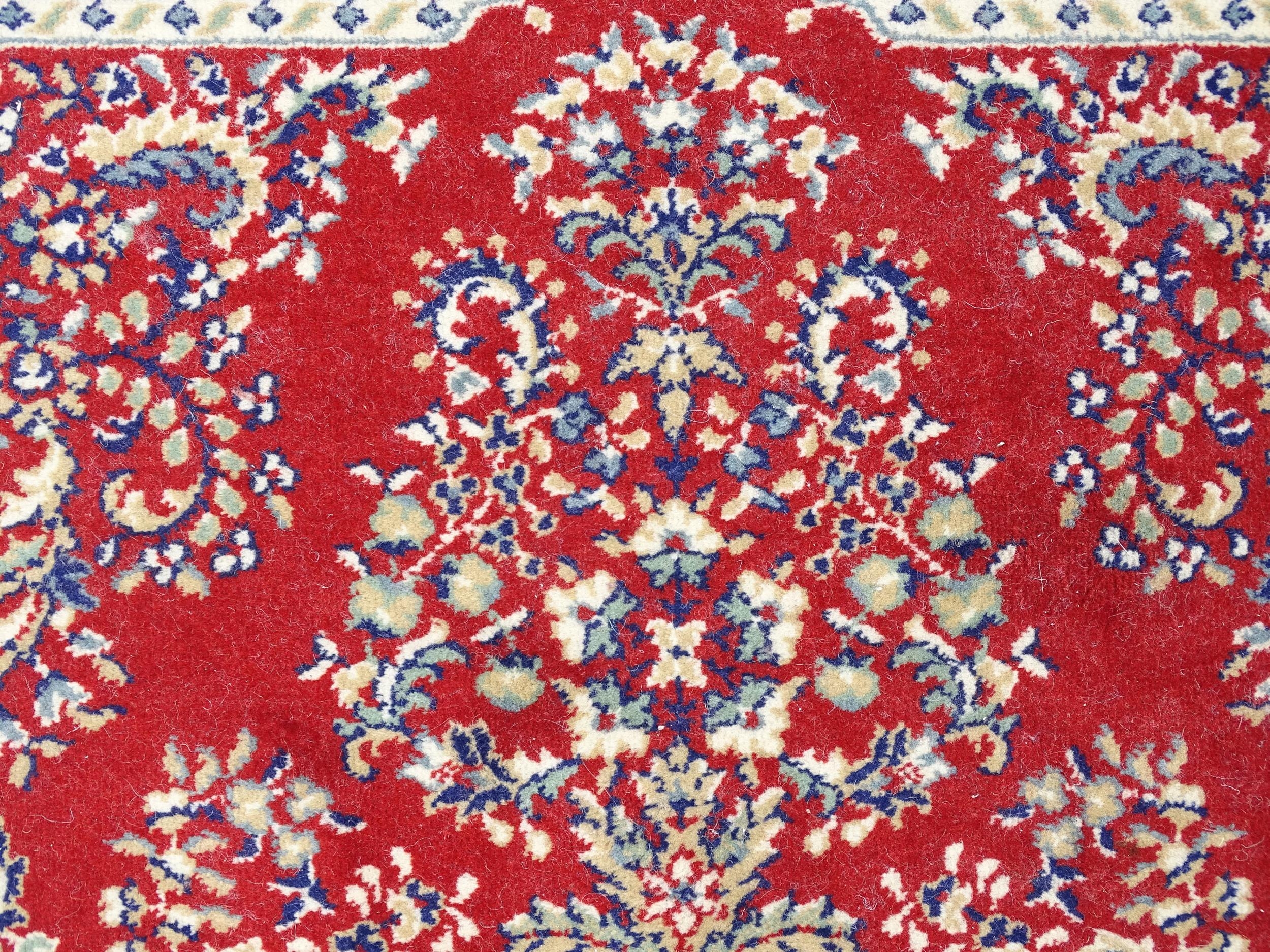 Carpet / Rug : A red ground rug with central cream and blue vignette, decorated with floral and - Image 4 of 6