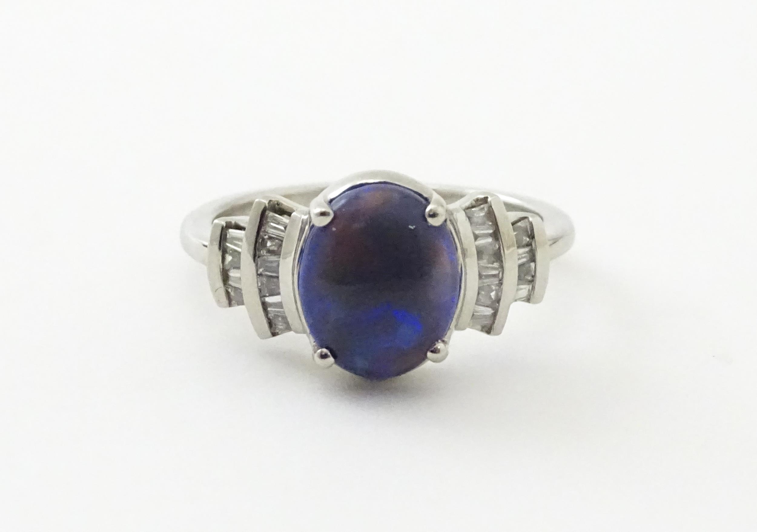 A platinum ring set with central black opal cabochon flanked by diamonds in an Art deco style