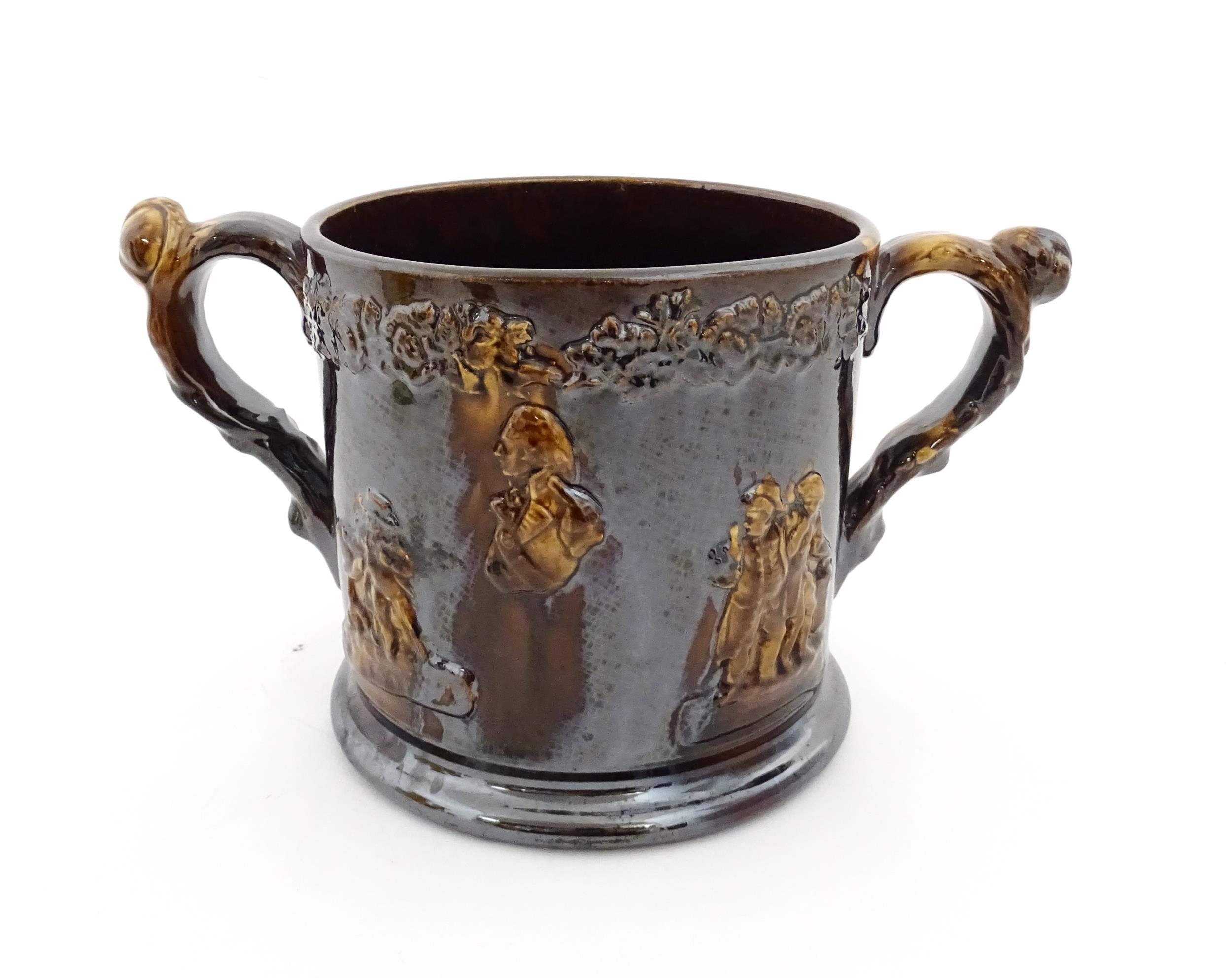 A large Staffordshire treacle glazed frog loving cup decorated in relief with depictions of