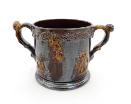 A large Staffordshire treacle glazed frog loving cup decorated in relief with depictions of