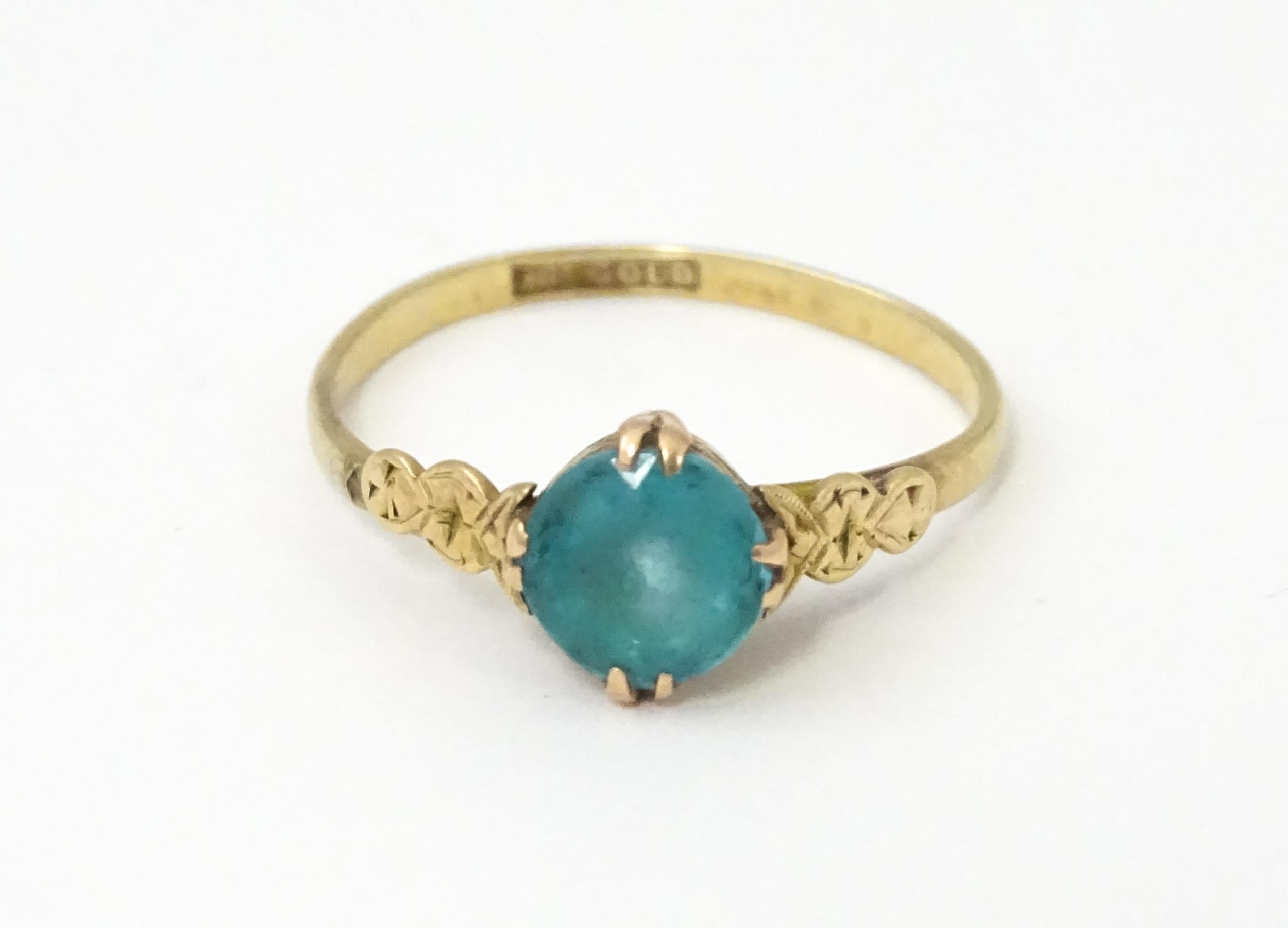 A 9ct gold ring set with aqua coloured glass to centre with engraved detail to shoulders. Ring