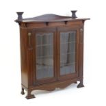 An Art Nouveau mahogany cabinet with a shaped upstand and two leaded glass doors with floral