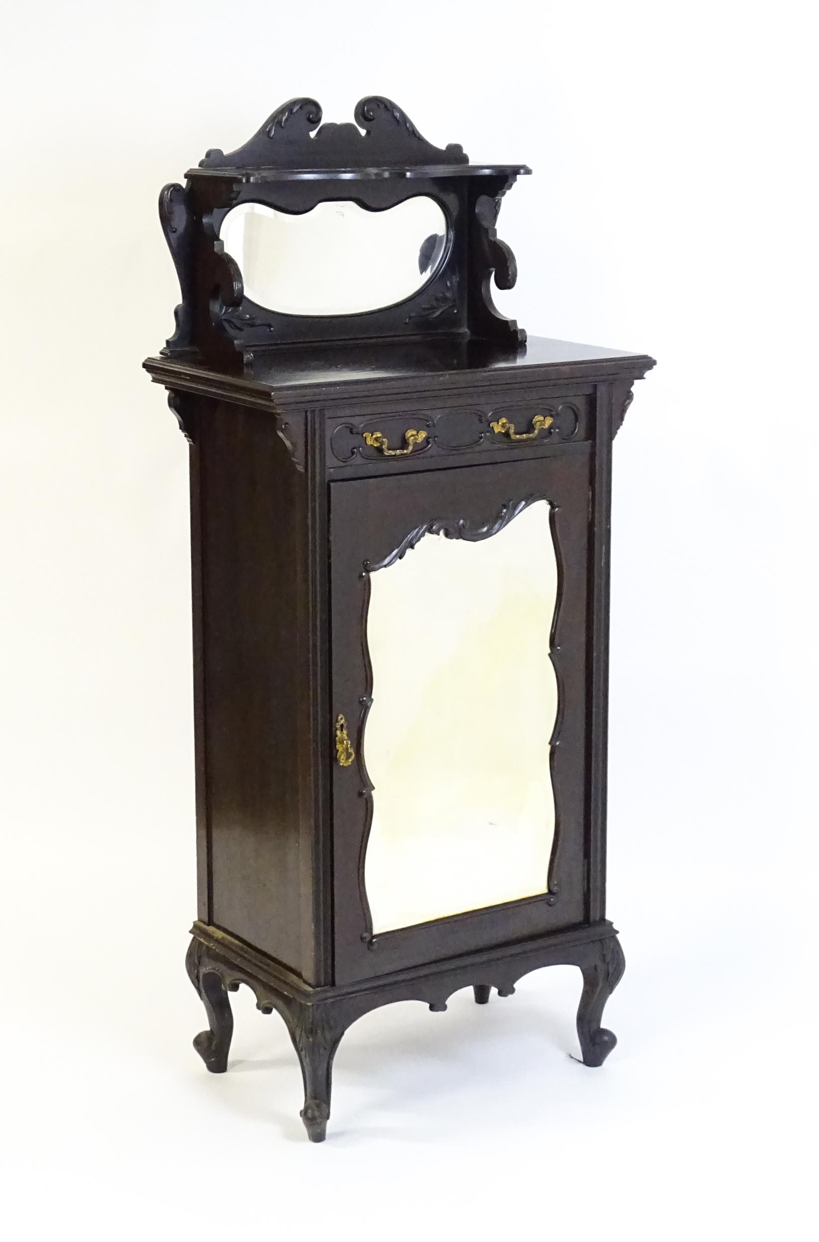 A late Victorian ebonised side cabinet with a mirrored upstand, a moulded top and a single frieze